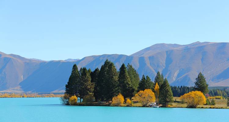 Turquoise alpine lake edged by pine trees with barren mountains rising behind.