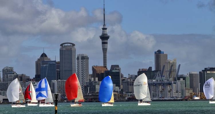 Segelboote mit bunten Segeln vor einer Stadtskyline.