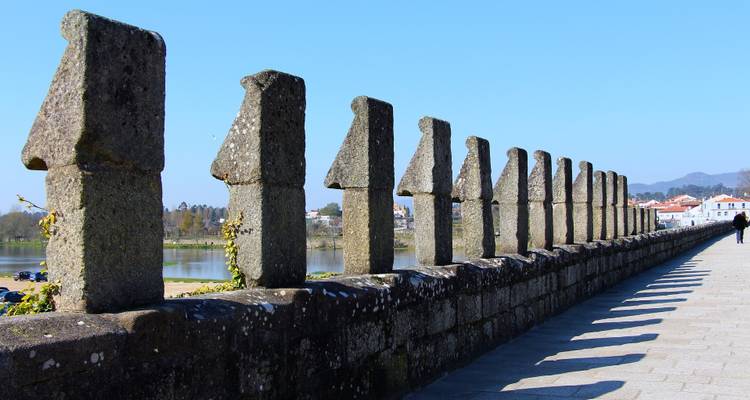 Stone bridge lined with sculpted pillars overlooking a calm river on a clear day.