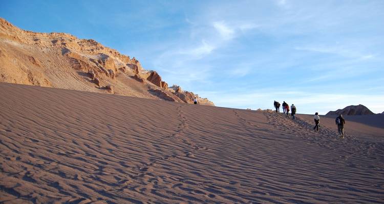 Personas caminando a través de vastas dunas de arena en un paisaje desértico.