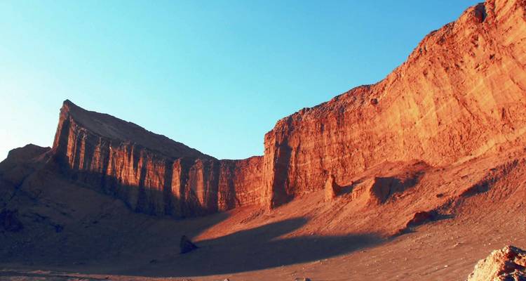 Una pared de acantilado escarpada iluminada por el sol en una zona desértica.