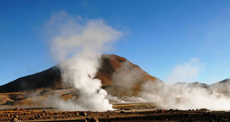 Geysers dégageant de la vapeur avec une montagne en arrière-plan.