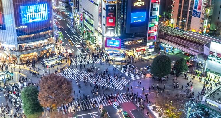 Vue aérienne nocturne du carrefour de Shibuya animé, entouré de gratte-ciel brillamment illuminés et de panneaux publicitaires au néon à Tokyo.