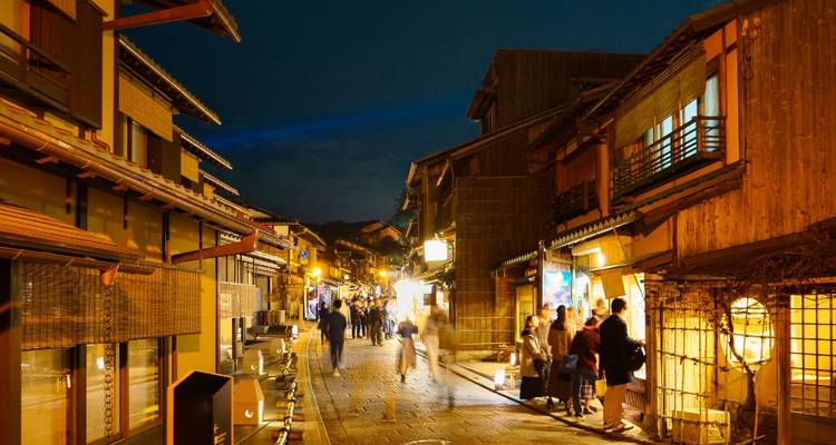 Scène de soirée atmosphérique avec des ruelles étroites éclairées par des lanternes et des maisons en bois machiya dans le quartier de Gion à Kyoto avec des piétons flous.