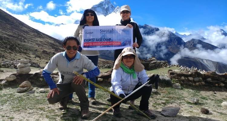 Grupo sosteniendo pancarta en el Campo Base del Everest con montañas de fondo.