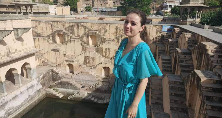 Woman in turquoise dress standing beside the multi-level stepwell of Panna Meena ka Kund near Jaipur.