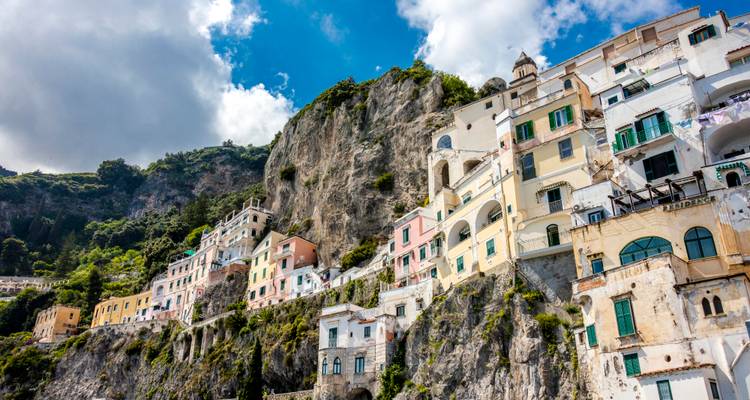 Les maisons colorées accrochées à flanc de falaise à Amalfi s'agrippent à la roche calcaire au-dessus de la mer bleue sous des nuages épars.