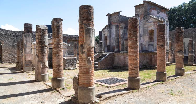 Une rangée de colonnes en brique se dresse au milieu de bâtiments partiellement restaurés dans les ruines de Pompéi.