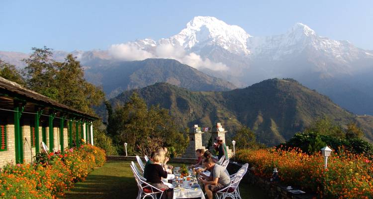 Personas cenando al aire libre con vista al Himalaya.