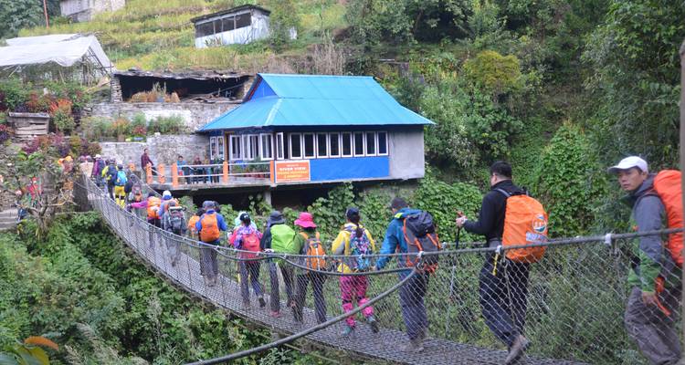 Wandergruppe überquert eine Hängebrücke in Richtung eines kleinen Hauses.
