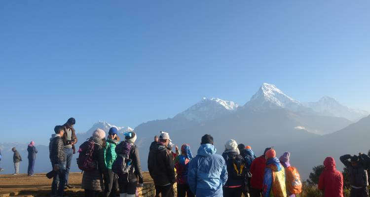 Gruppe von Menschen, die schneebedeckte Berge von einem Hügel aus betrachten.