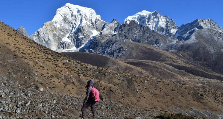Person, die in einer bergigen Landschaft mit schneebedeckten Gipfeln im Hintergrund wandert.