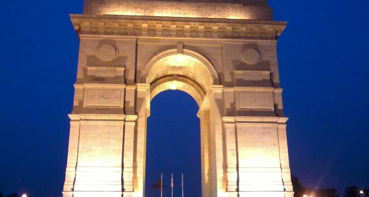 India Gate illuminated at night with blue sky background.