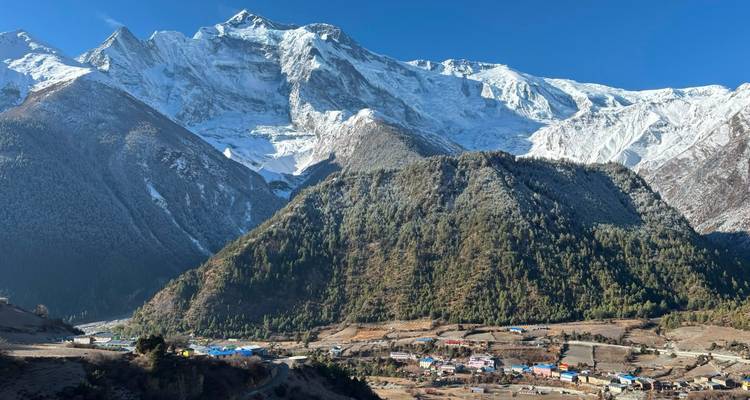 Snow-draped Himalayan massif rises above a patchwork valley dotted with colourful village roofs.