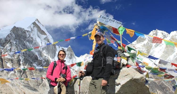 Dos personas posando en el Campo Base del Everest con banderas de oración.