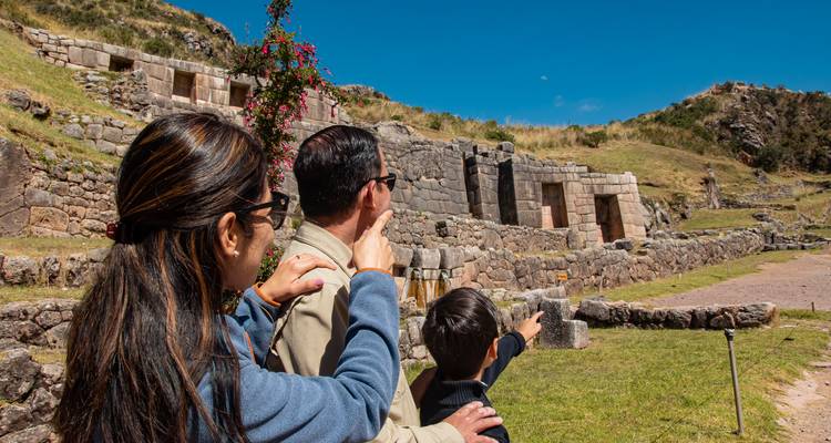 La familia señala las antiguas ruinas de piedra en el Valle Sagrado bajo un cielo azul despejado.