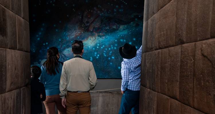 Los visitantes contemplan la proyección del cosmos lleno de estrellas en el pasillo del museo Inca débilmente iluminado.