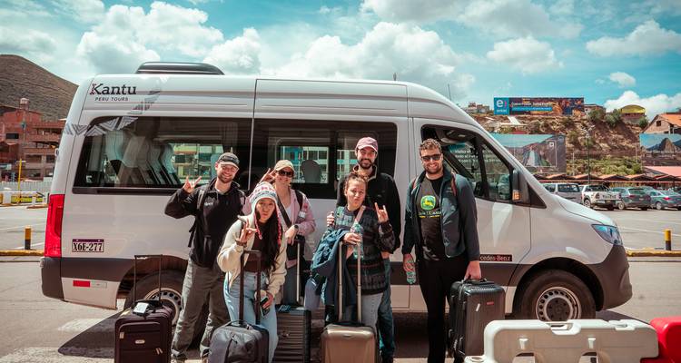 El grupo de turismo está de pie frente a una minibús en el estacionamiento, haciendo señas de paz y listos para partir.