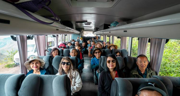 Pasajeros sentados dentro del autobús de tour sonriendo hacia la cámara mientras comienza el viaje.
