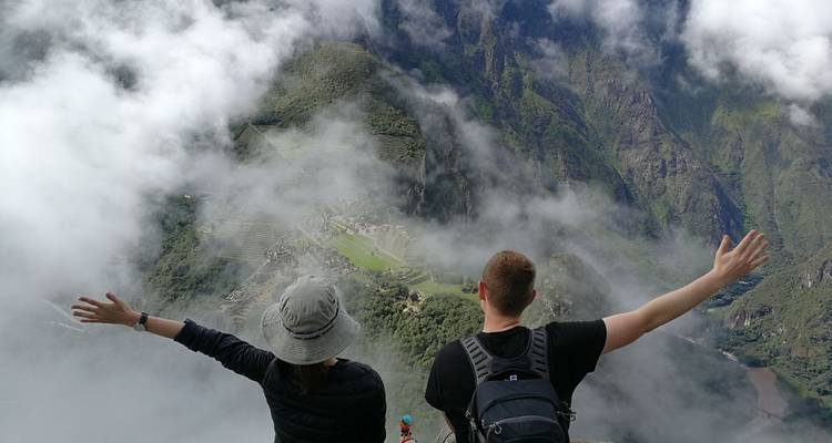 Pareja con los brazos levantados contemplando Machu Picchu nublado.