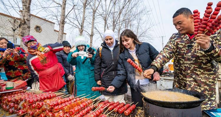 Los visitantes prueban coloridas brochetas de espino blanco cubiertas de azúcar en un animado puesto callejero de comida de invierno al aire libre.