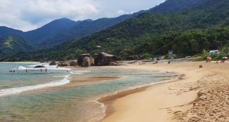 Plage avec des montagnes en arrière-plan et des gens qui nagent.