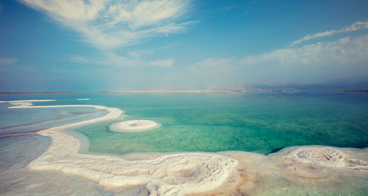 Vue panoramique des eaux vert émeraude de la mer Morte bordées de dépôts de sel blanc tourbillonnants sous un ciel voilé