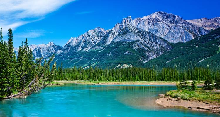 Turquoise river flowing beneath rugged snow-capped peaks and dense pine forest in the Canadian Rockies