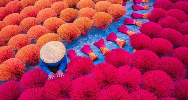 Overhead shot of a worker arranging vibrant red and orange incense sticks in Vietnam.