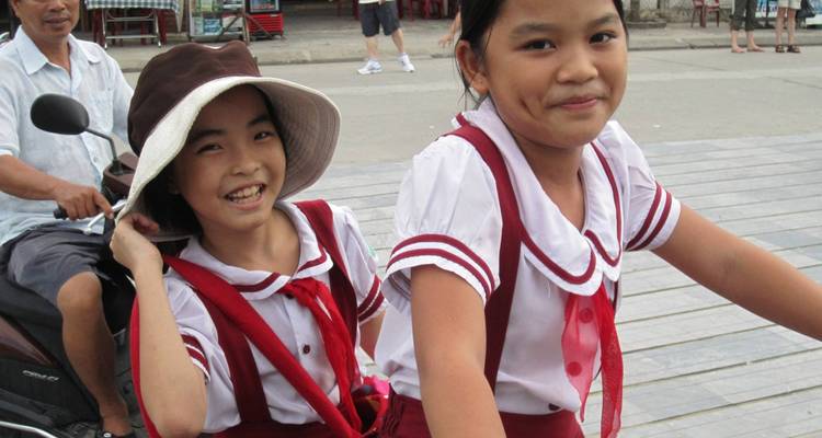 Deux filles en uniforme qui font du vélo dans une rue.