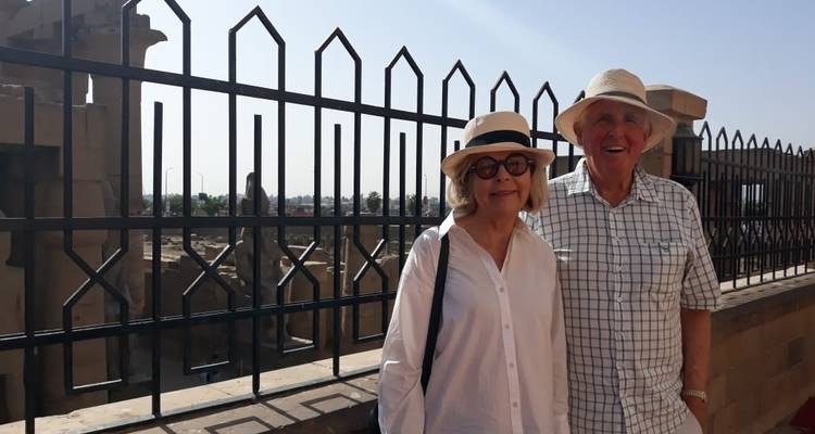 Pareja sonriente posando junto a una valla en un sitio histórico.