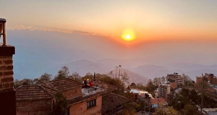 Sol naranja cayendo sobre las colinas del Himalaya envueltas en niebla y los tejados rústicos del pueblo de Nagarkot.