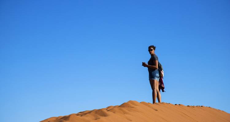 Persoon die op een zandduinen staat onder een heldere blauwe lucht.