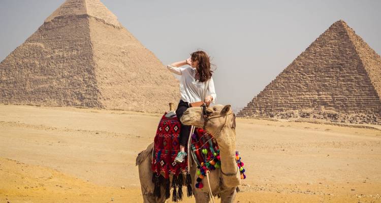 A person on a camel with the Pyramids of Giza in the background.