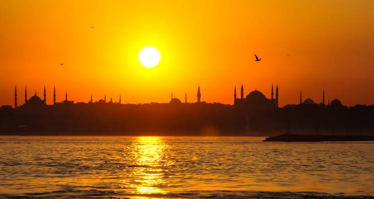 Sonnenuntergang über einer Stadtlandschaft mit Moscheen und Minaretten.