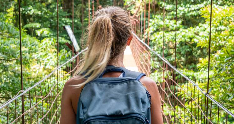 Vue arrière d'une randonneuse avec sac à dos traversant un pont suspendu en jungle