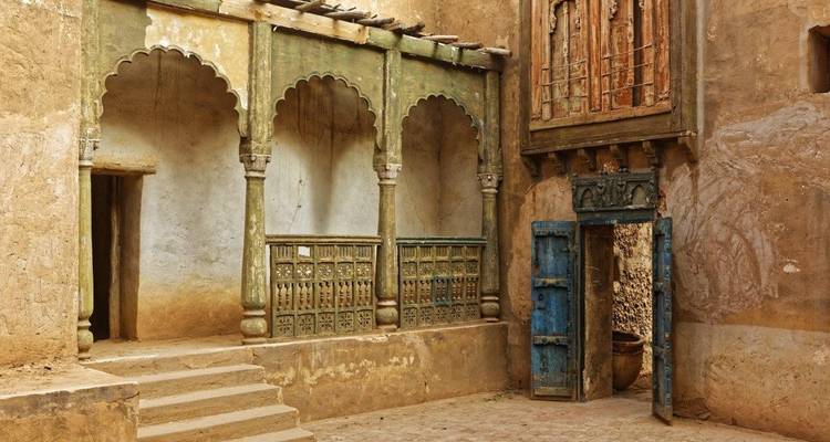 Une cour traditionnelle et rustique avec des colonnes ornées et de vieilles portes.