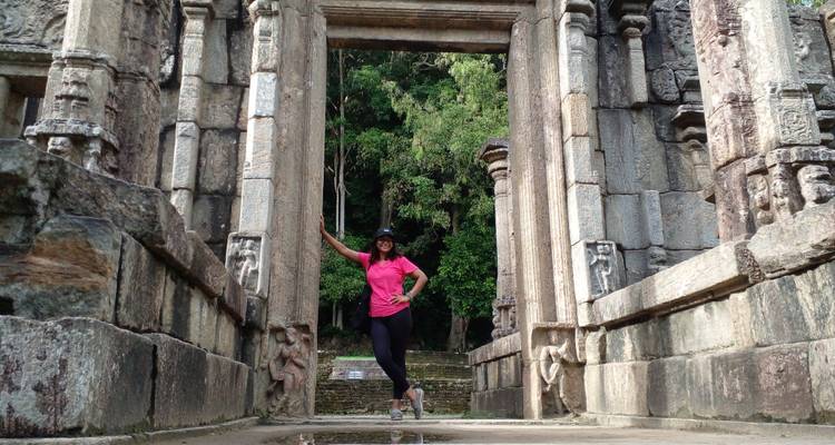 Traveler posing in ancient stone doorway of historic ruins surrounded by lush green trees.