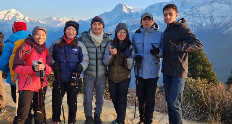 Groupe de personnes sur un sentier de montagne avec des bâtons de randonnée, pics enneigés en arrière-plan.