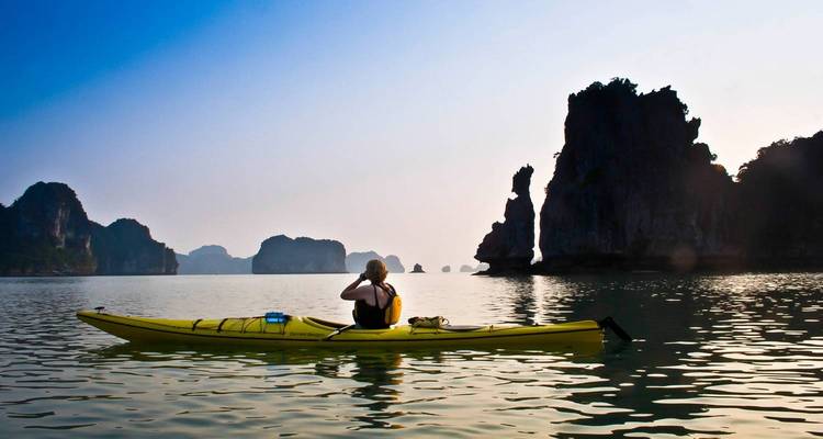 Mujer navegando en kayak en aguas serenas con formaciones kársticas de piedra caliza en la distancia.