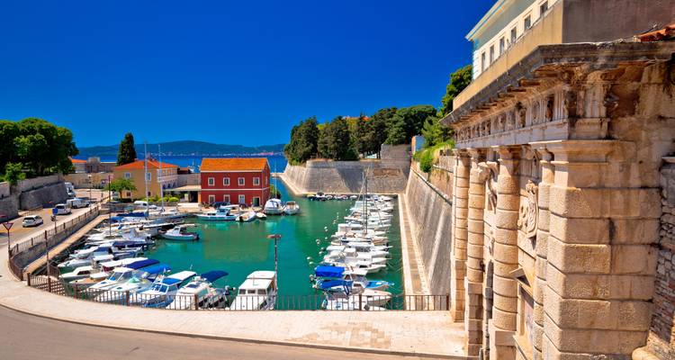 Petite marina croate aux eaux turquoise, bateaux amarrés et portail en pierre historique