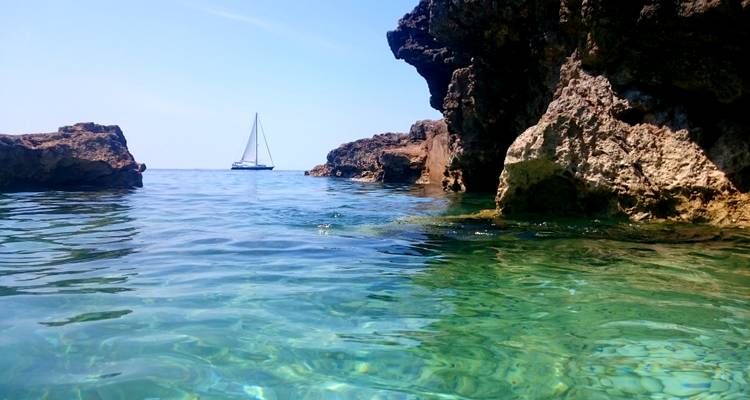 Eau cristalline de l'Adriatique entre des falaises rocheuses avec un voilier au loin