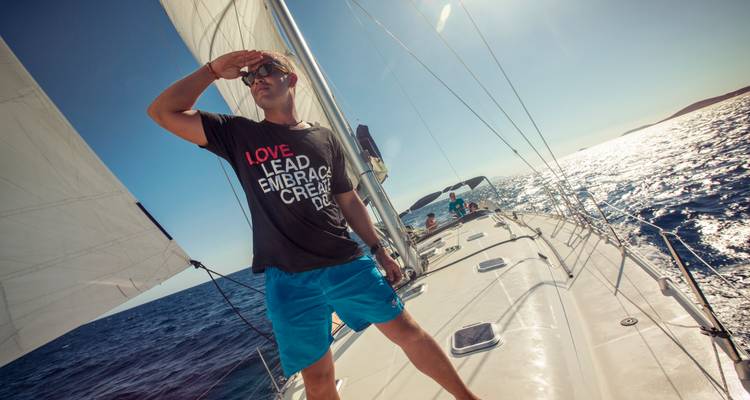 Un homme debout sur le pont d'un yacht à voiles regardant vers l'horizon par une journée ensoleillée