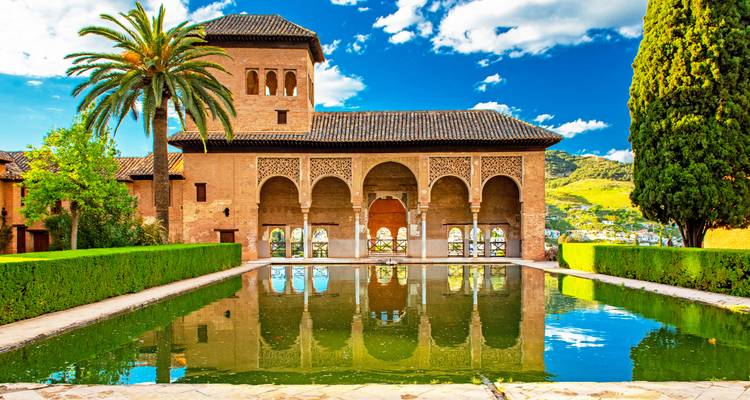 Área de jardín histórico con una piscina que refleja un edificio ornamentado.