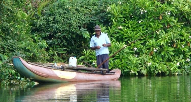 Een man die op een kleine boot staat met een hengel in zijn hand, omringd door weelderig groen.