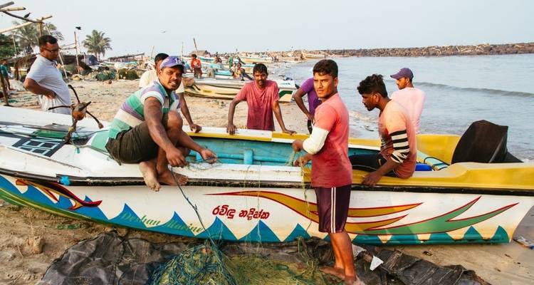 Mannen die werken aan een kleurrijke boot met visnetten op een strand.