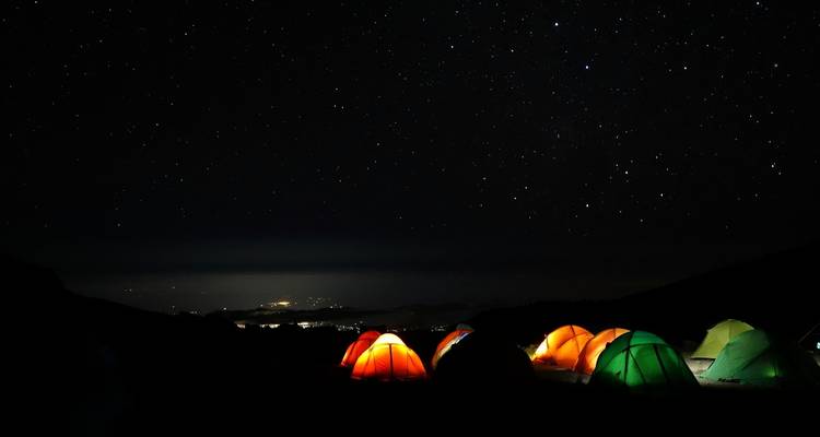 Night sky with colorful tents illuminated at a campsite.