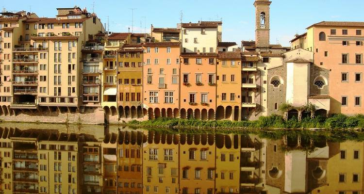 Fila de coloridos edificios renacentistas reflejándose perfectamente en las aguas tranquilas del río Arno.