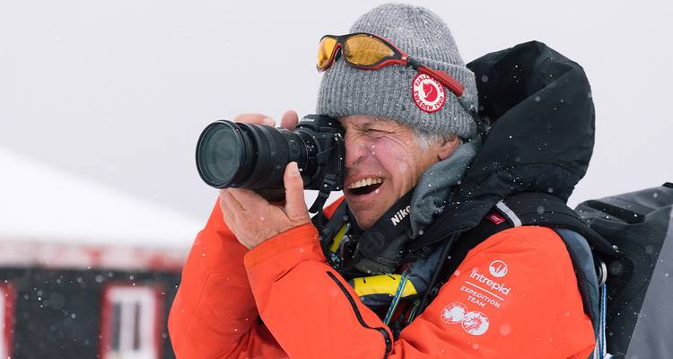 Een expeditie fotograaf in een oranje parka fotografeert vrolijk wilde dieren terwijl er sneeuwvlokken vallen.