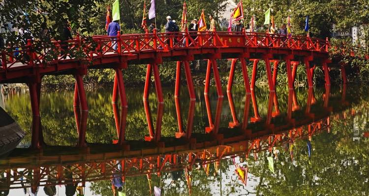 Puente de madera rojo sobre un lago sereno.